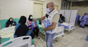 (FILES) In this file photo taken on October 26, 2022, a man hands out water bottles to people waiting on patients  infected in an outbreak of Vibrio cholera, receiving treatment in a mosque hall converted into a field hospital in the town of Bebnine in the Akkar district in north Lebanon. - Last month Lebanon recorded its first cholera case since 1993, in the nearby Syrian refugee camp of Rihaniye, weeks after an outbreak in Syria, which lies about 20 kilometres (12 miles) away. Over a quarter of the country's more than 400 recorded cases are from  Bebnine, where people resort to unsafe water sources as the state fails to provide clean water. (Photo by Ibrahim CHALHOUB / AFP)